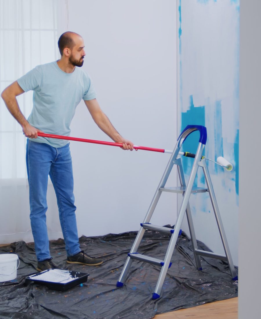 Masaking blue paint with roller brush dipped in white paint. Handyman renovating. Apartment redecoration and home construction while renovating and improving. Repair and decorating.